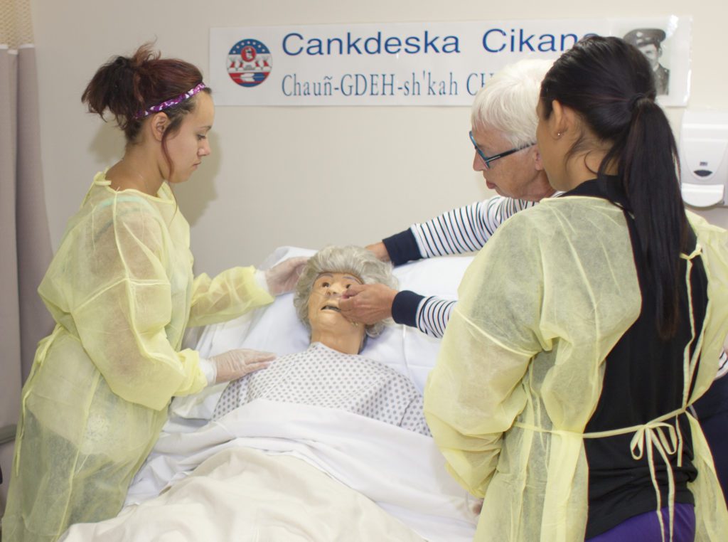 Nursing students receiving hands-on training with a training manequin and instructor.