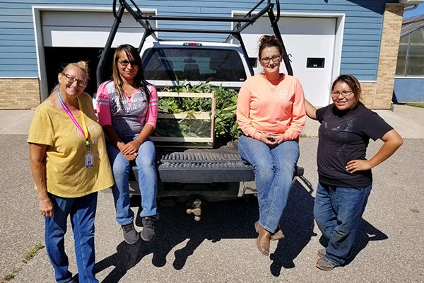 A group of woman next to a pickup truck with corn in the pickup box.